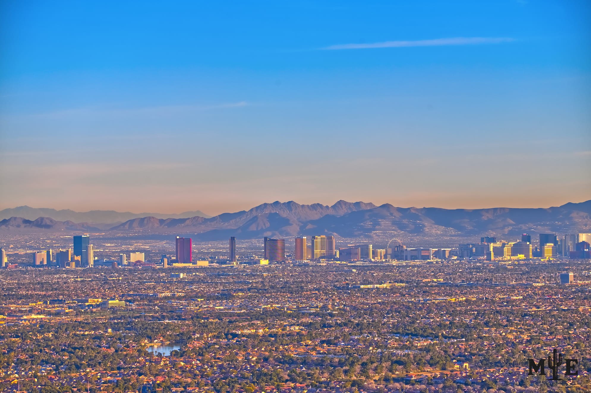 The Las Vegas Strip seen from Lone Mountain across the metropolitan valley, with distant hotels, layered mountains and a pastel blue sky.