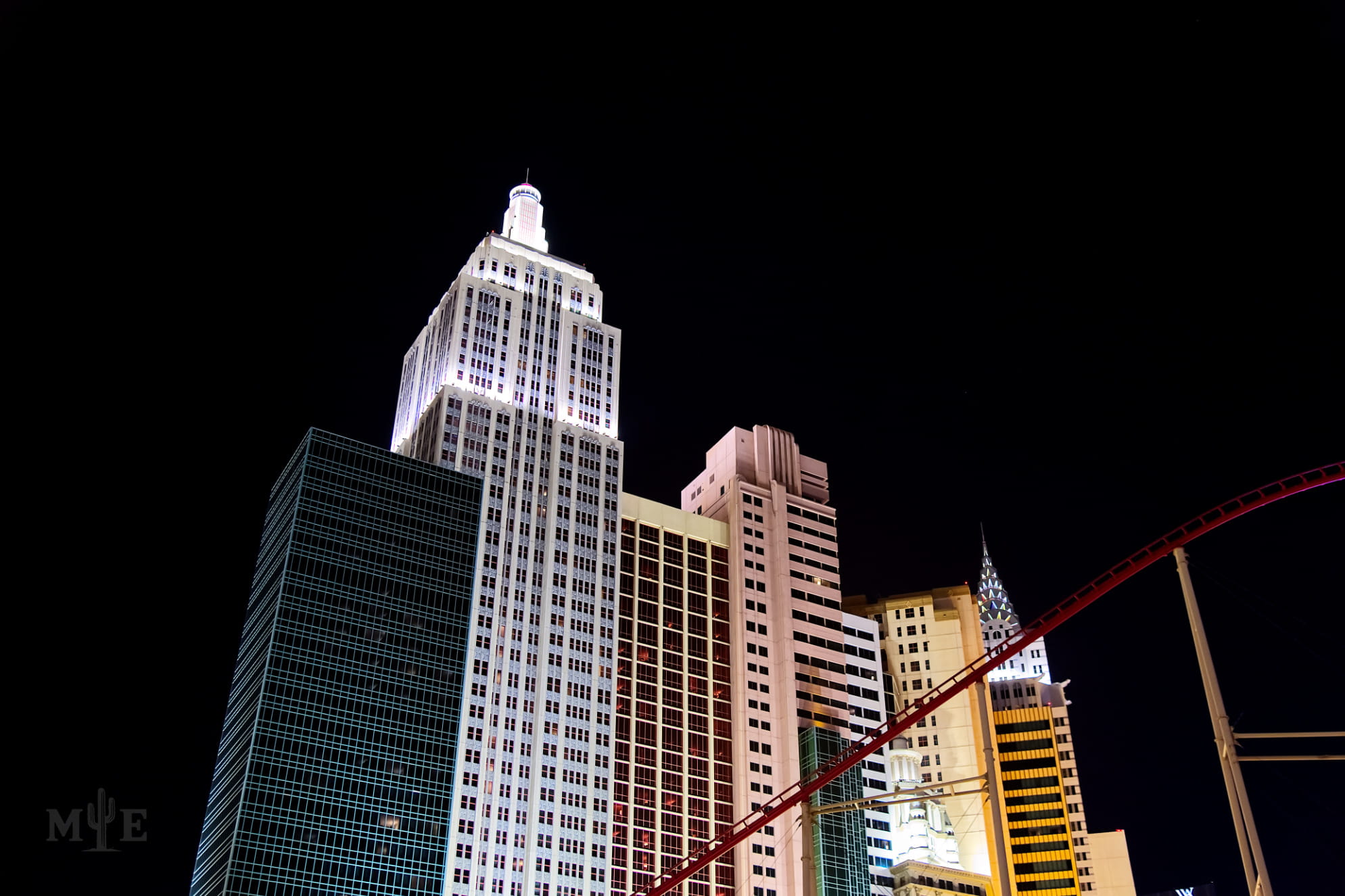 NY NY Hotel and Casino with a roller coaster sweeping by on a stark black night background.
