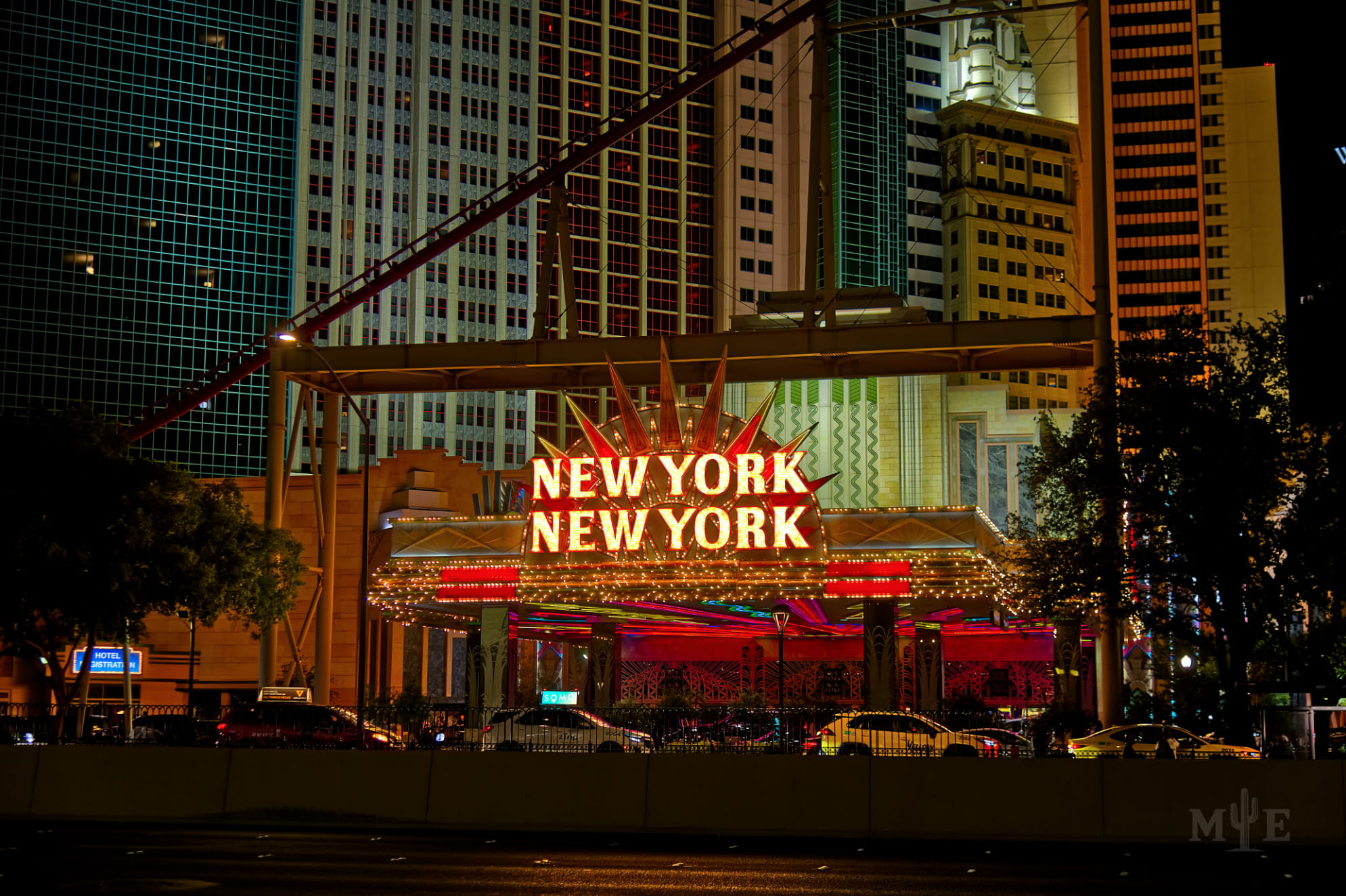 New York New York in neon, gleaming at night with the hotel and casino in the background. Foreground is in the shadows.