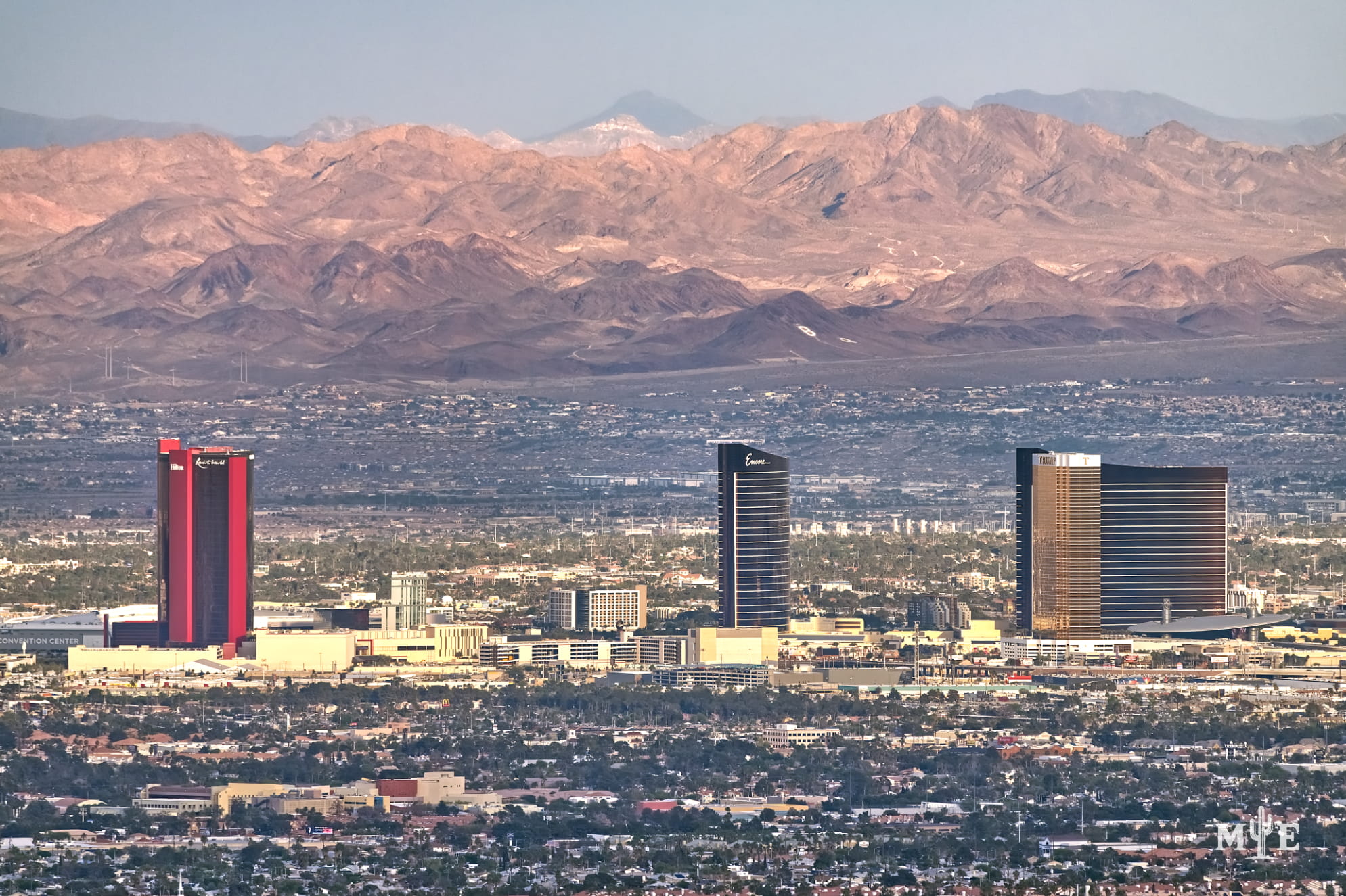Three distinctive hotels on The Strip spaced evenly apart, mountainous background, and densely populated city.