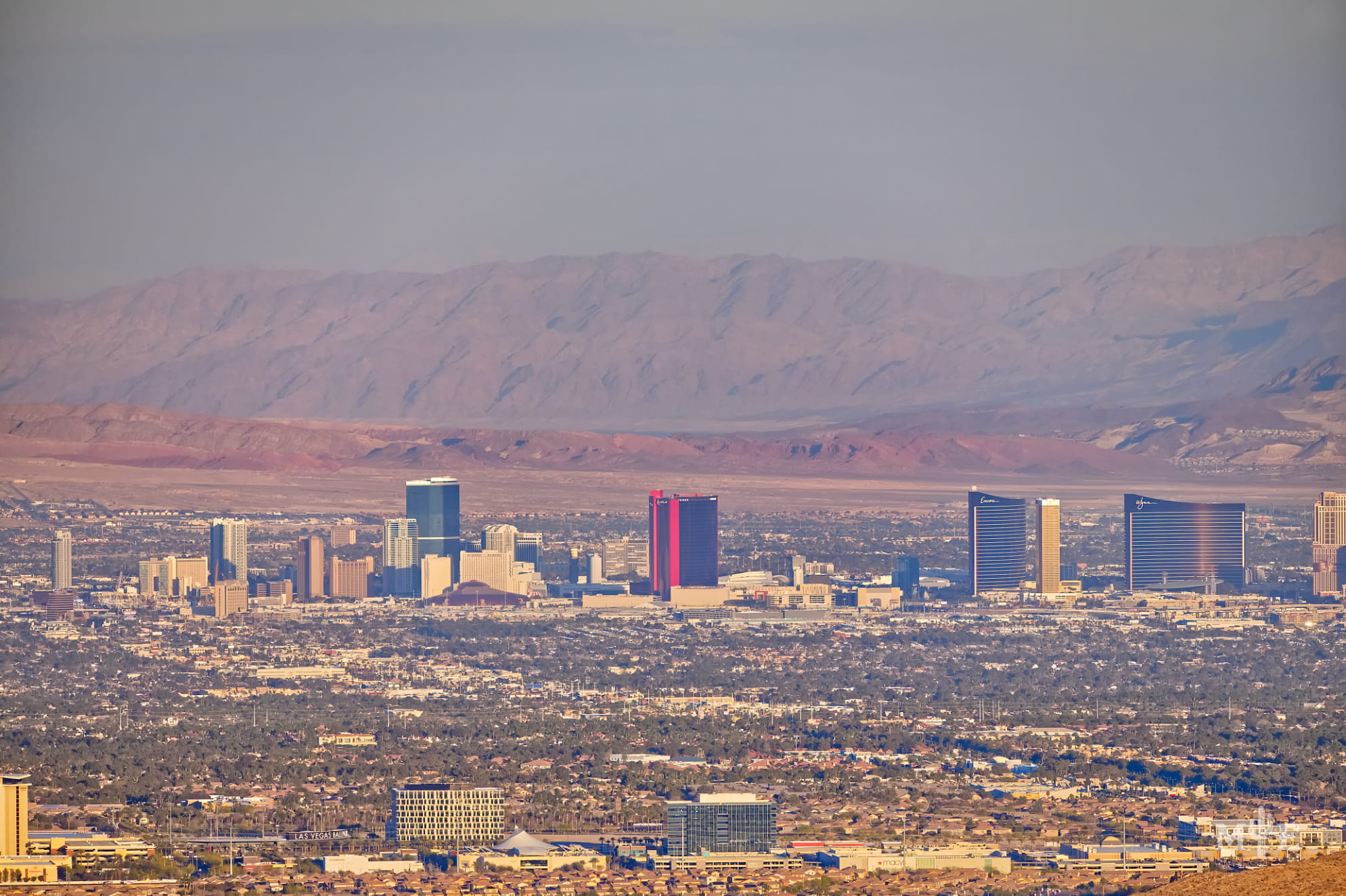 An array of hotels on The Strip in late afternoon rising above the populated, surrounding city desert landscape.