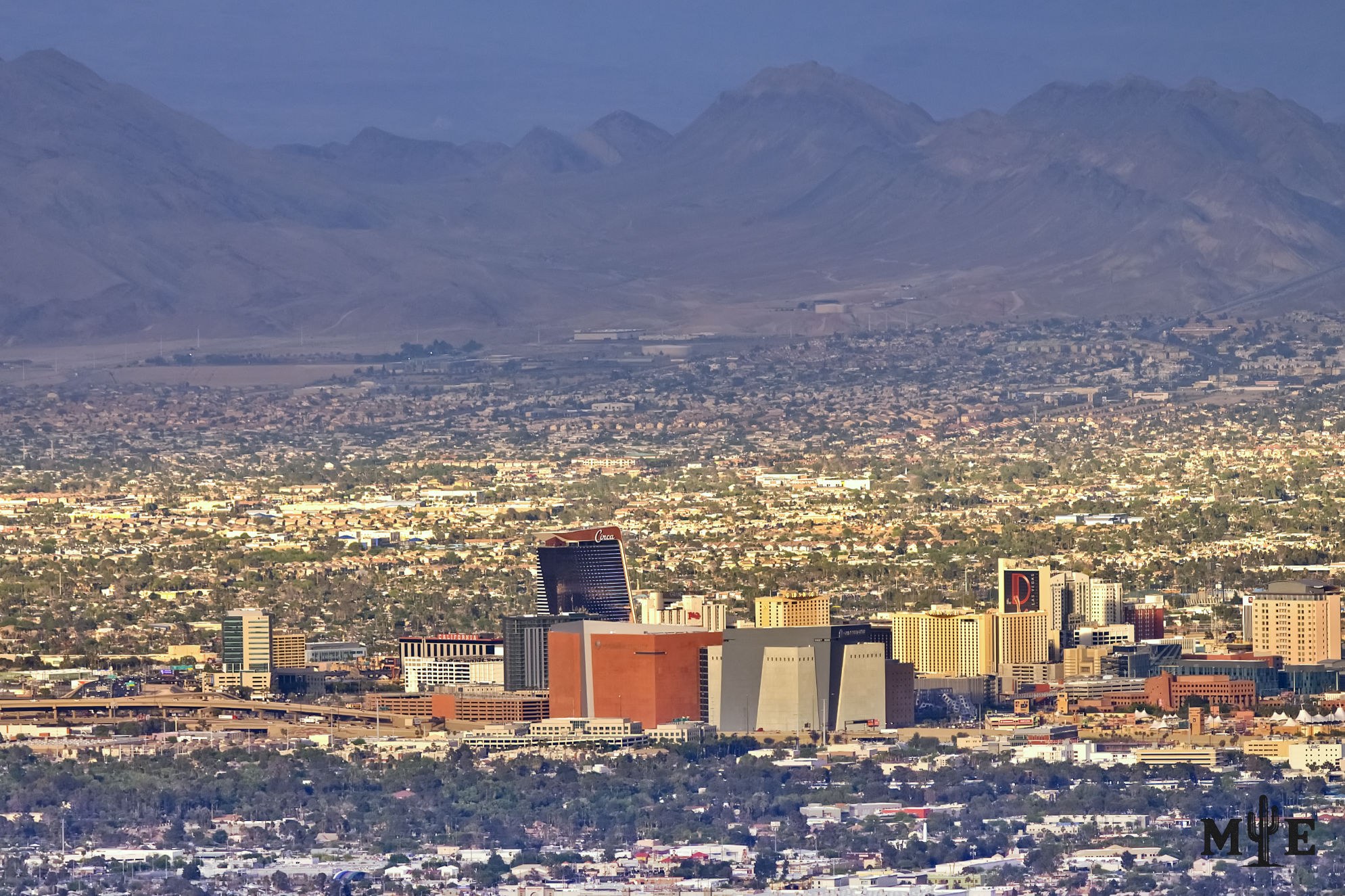 Telephoto view of downtown Las Vegas and casino towers, with dense city blocks and layered desert mountains behind them.