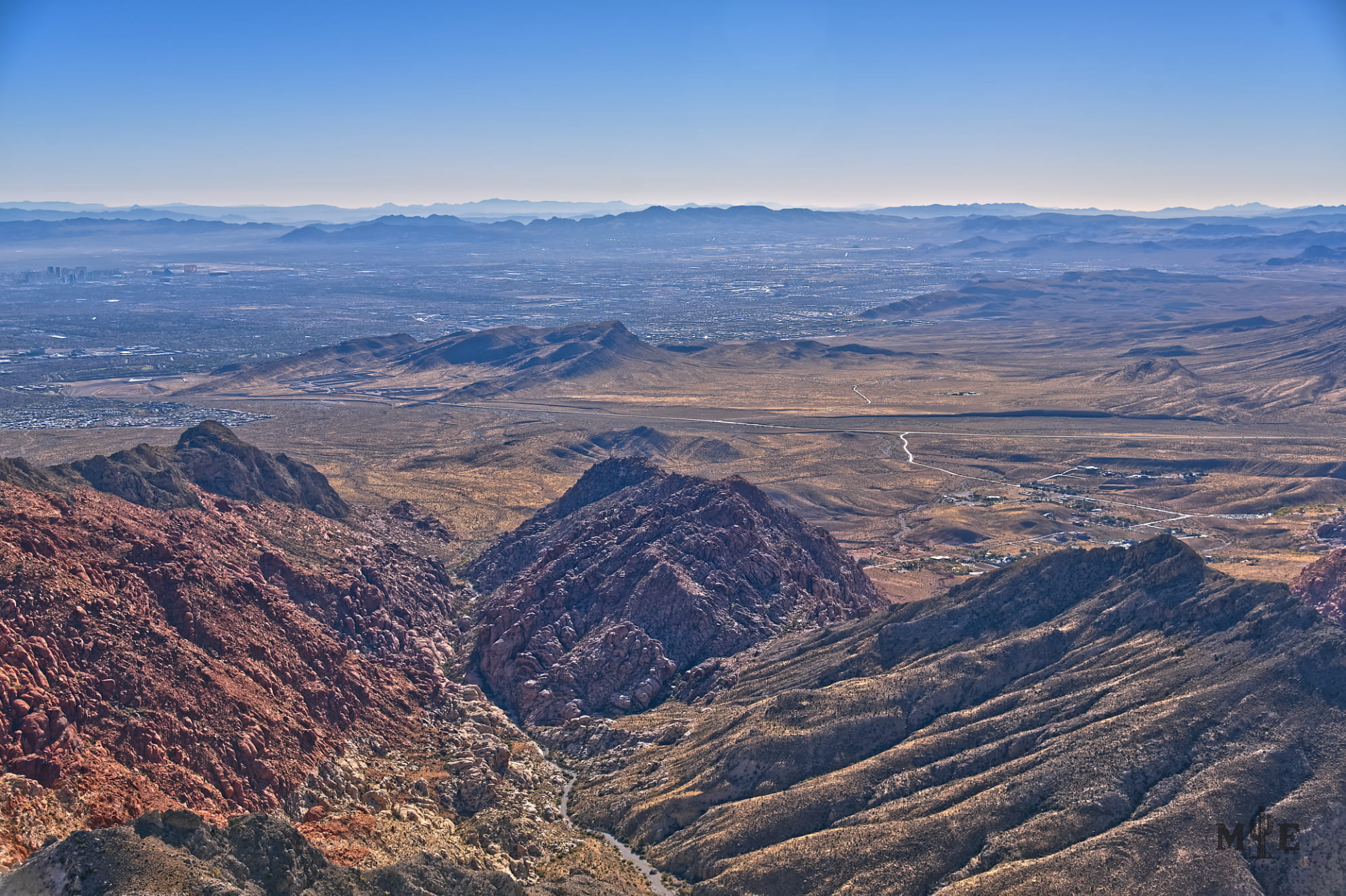 Very rugged Red Rock Canyon mountainous ravine with the Nevada desert, metro area, and pastel blue sky in the background.