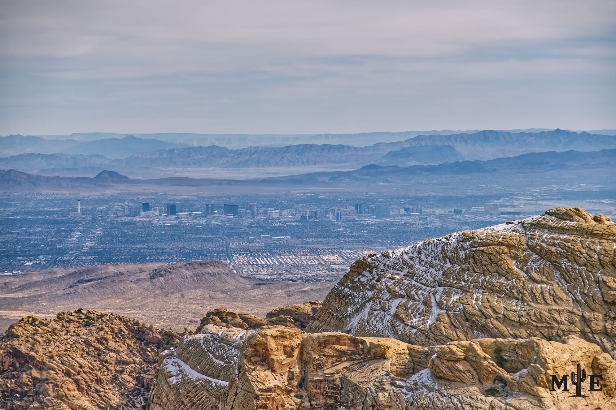 Snow-dusted sandstone mountains above Spring Valley & the Las Vegas urban basin, with distant ridges beneath layered clouds.