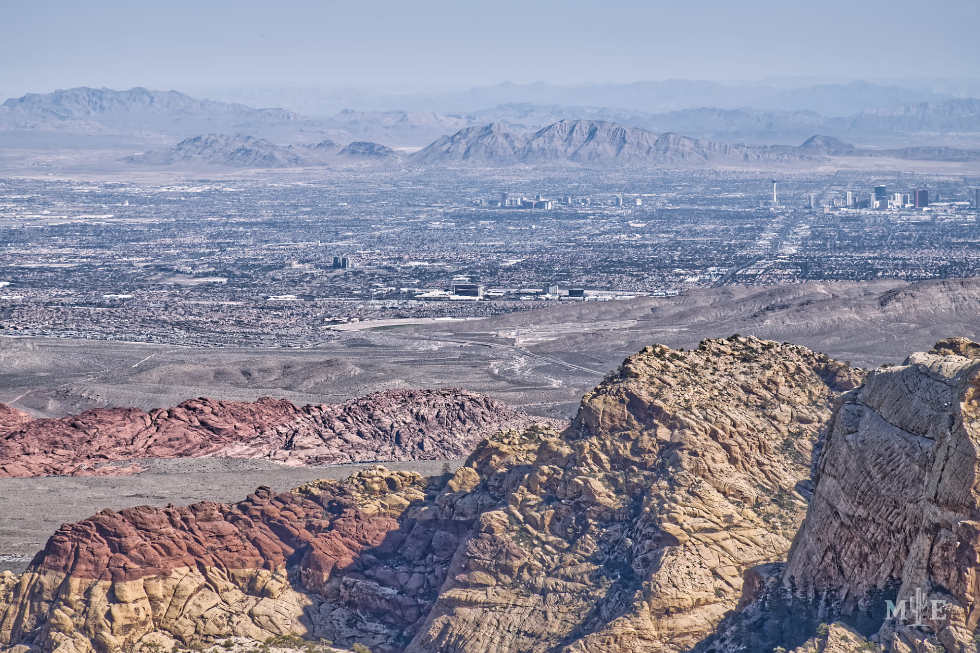Multi layered scene of jagged sandstone mountains and the Las Vegas valley below stretching far and wide.