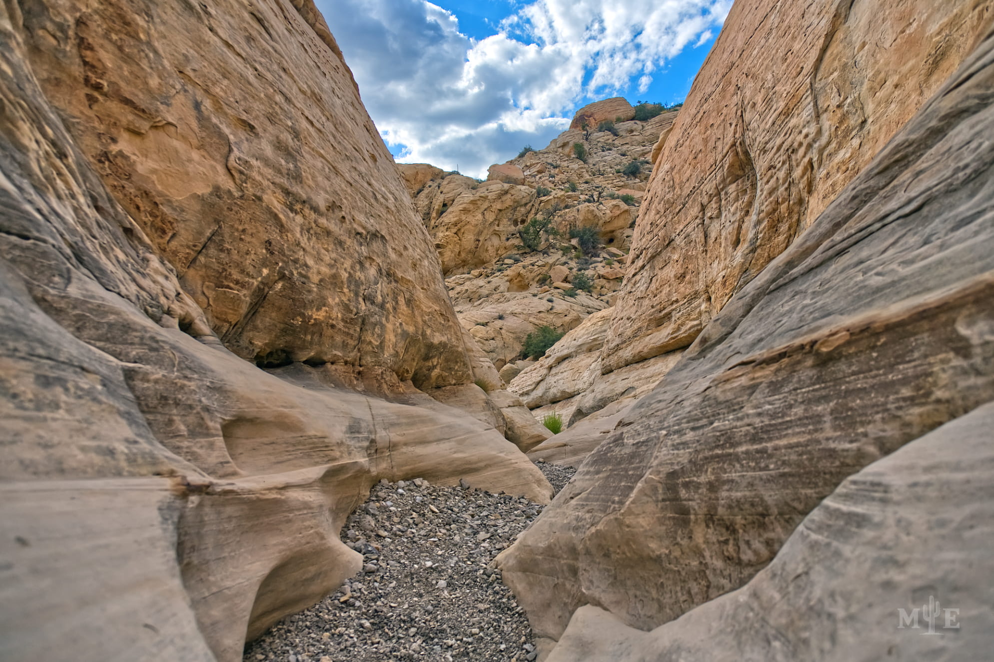 Sandstone rock clearly formed by years of water running through it. Cloudy blue sky in the background.