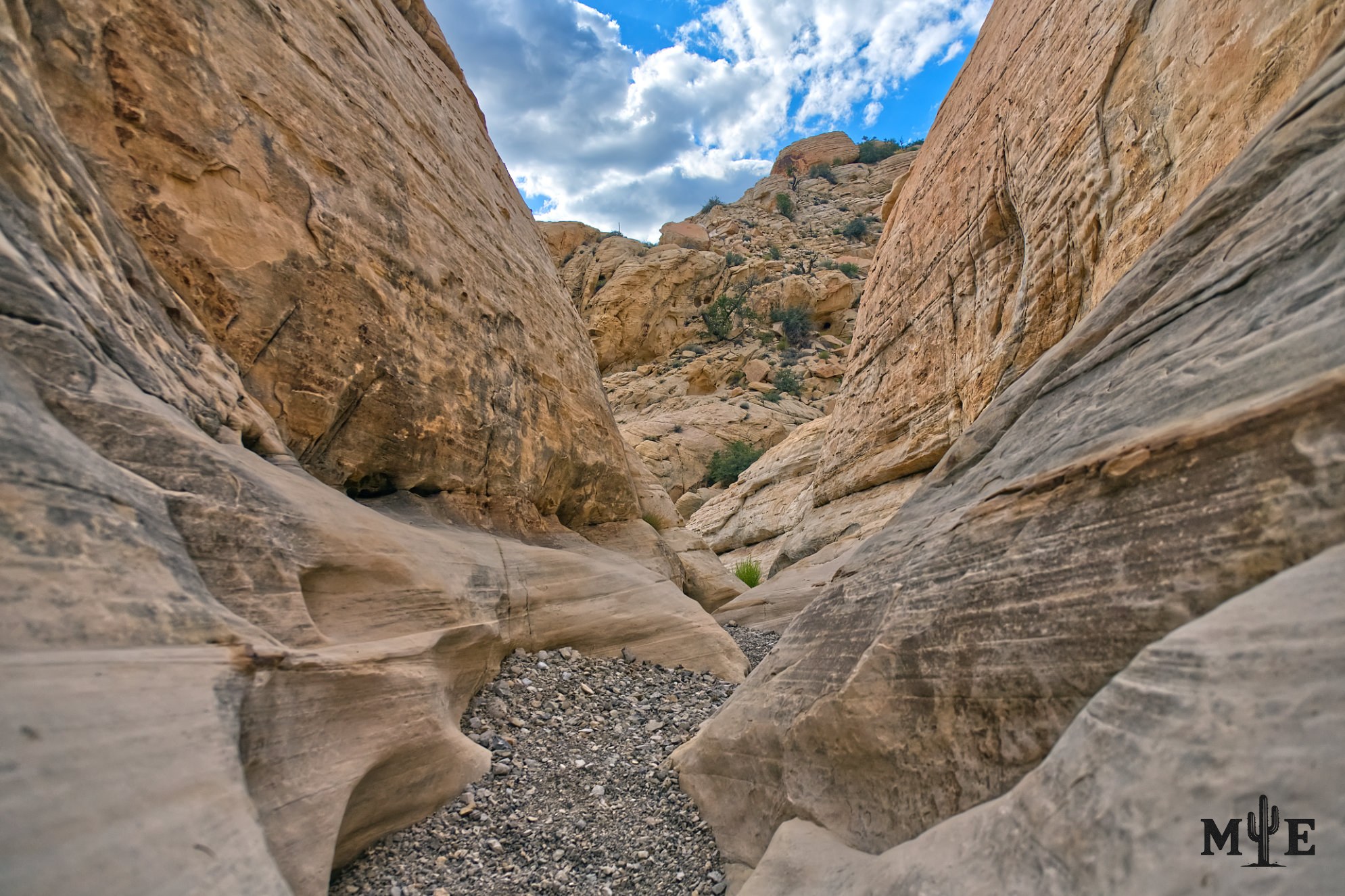 Sandstone rock clearly formed by years of water running through it. Cloudy blue sky in the background.