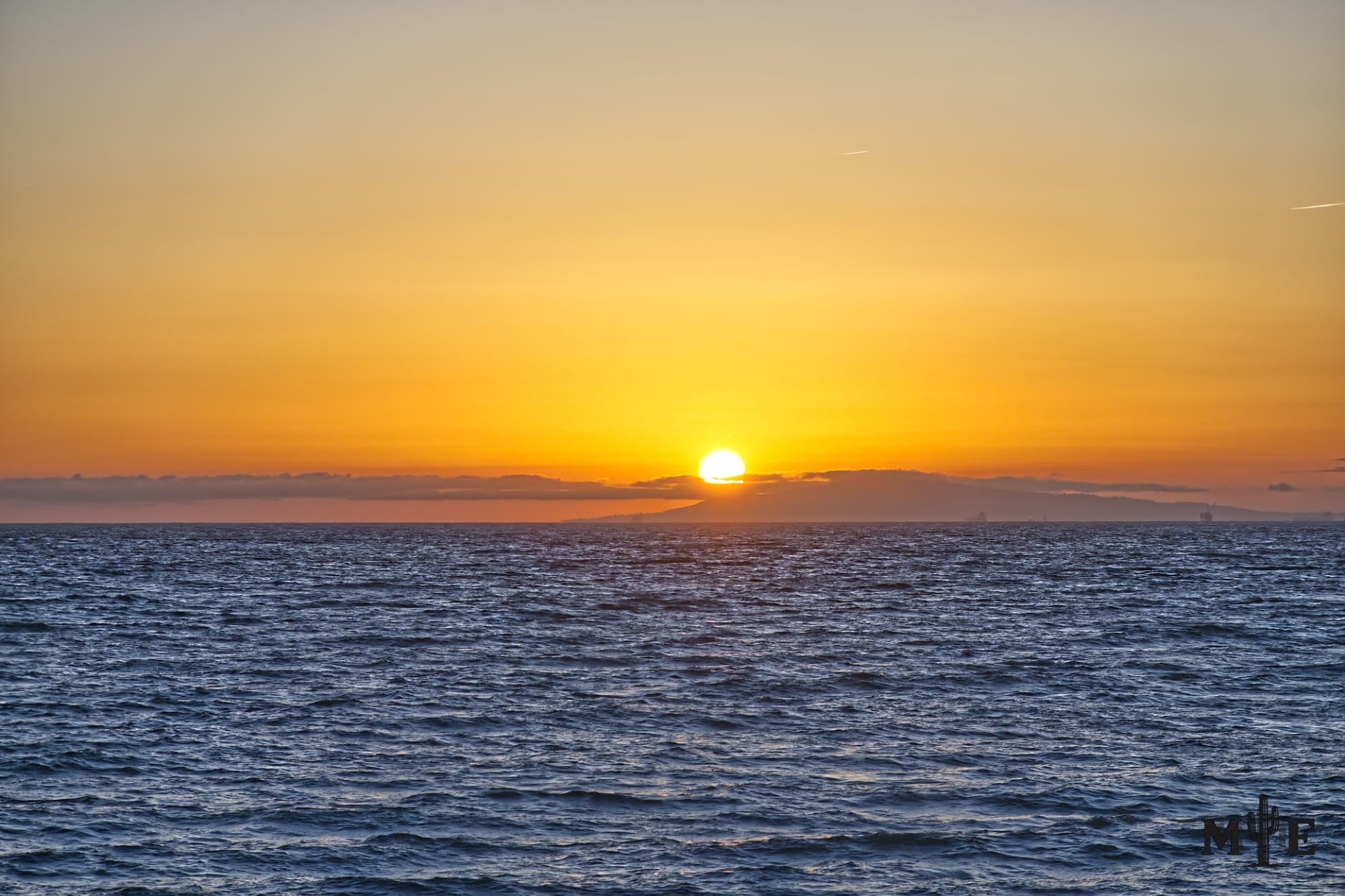Radiant yellow sunset above a deep blue ocean, with a clear horizon and only a few clouds where the sky meets the water.