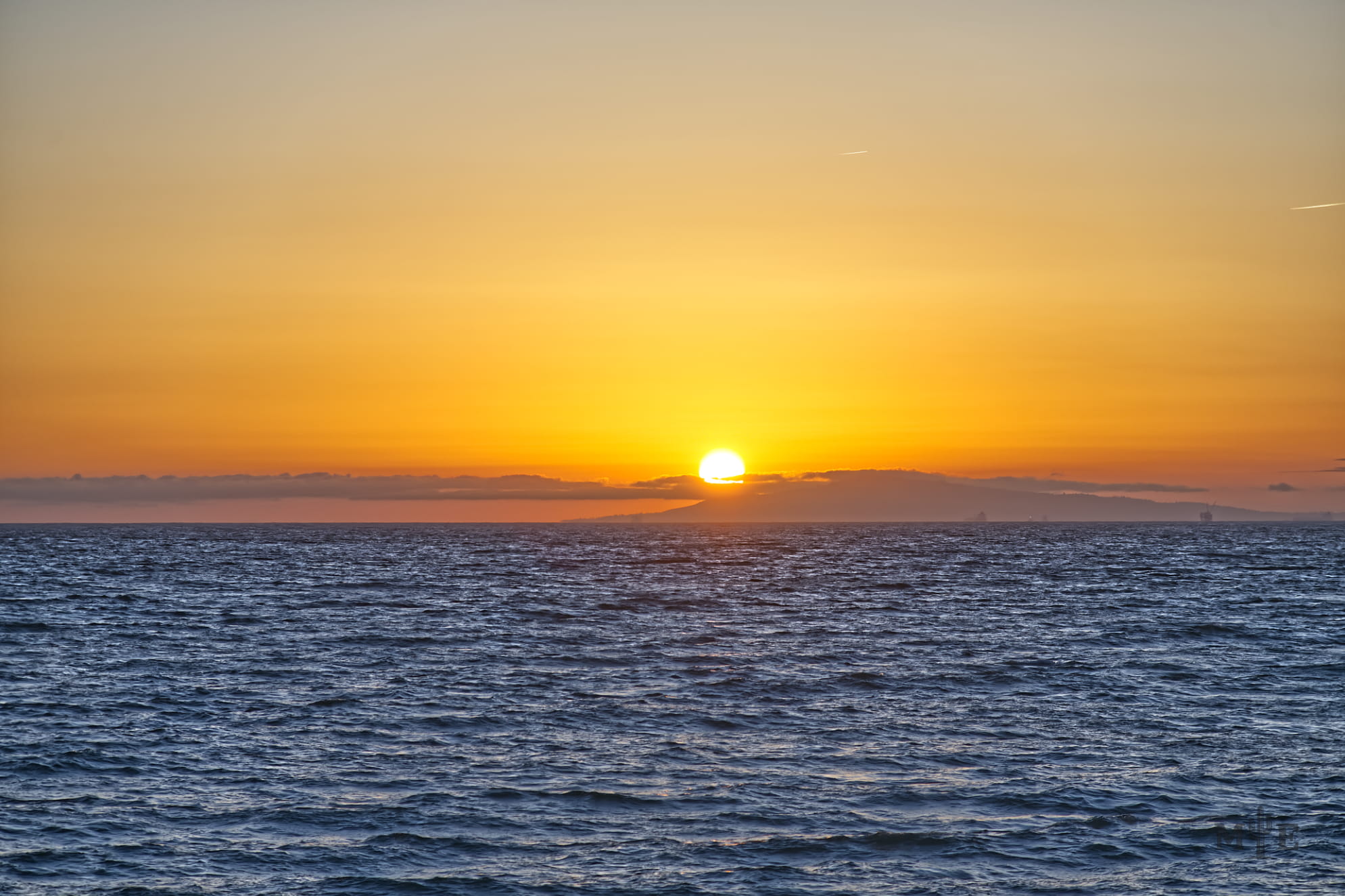 Bright yellow sunset casting across the sky with a deep blue ocean. Sky has minimal clouds where the water line begins.