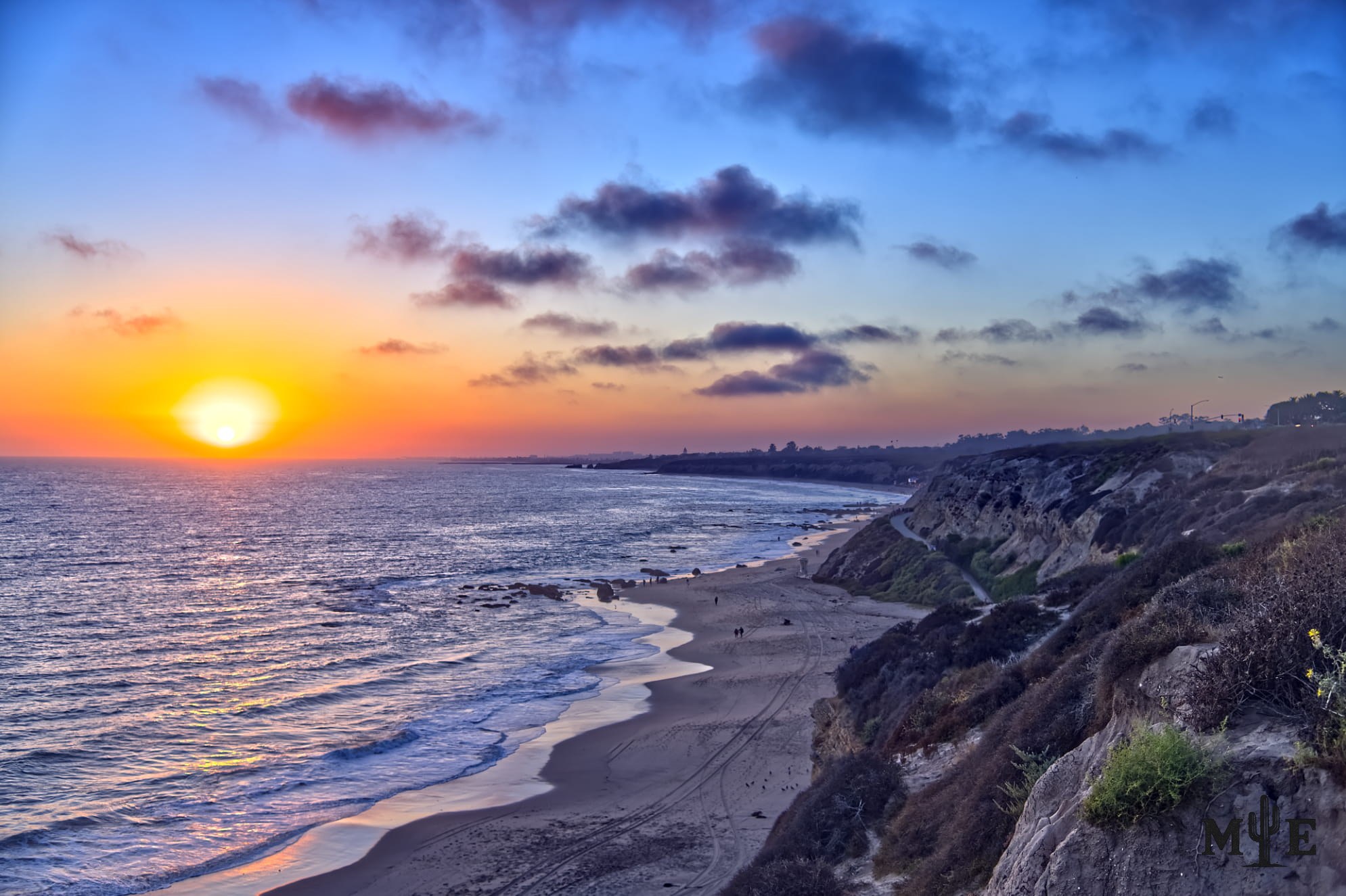 Marble-toned sunset over calm water at Emerald Bay in Orange County, with clouds and rugged coastal cliffs framing the shore.