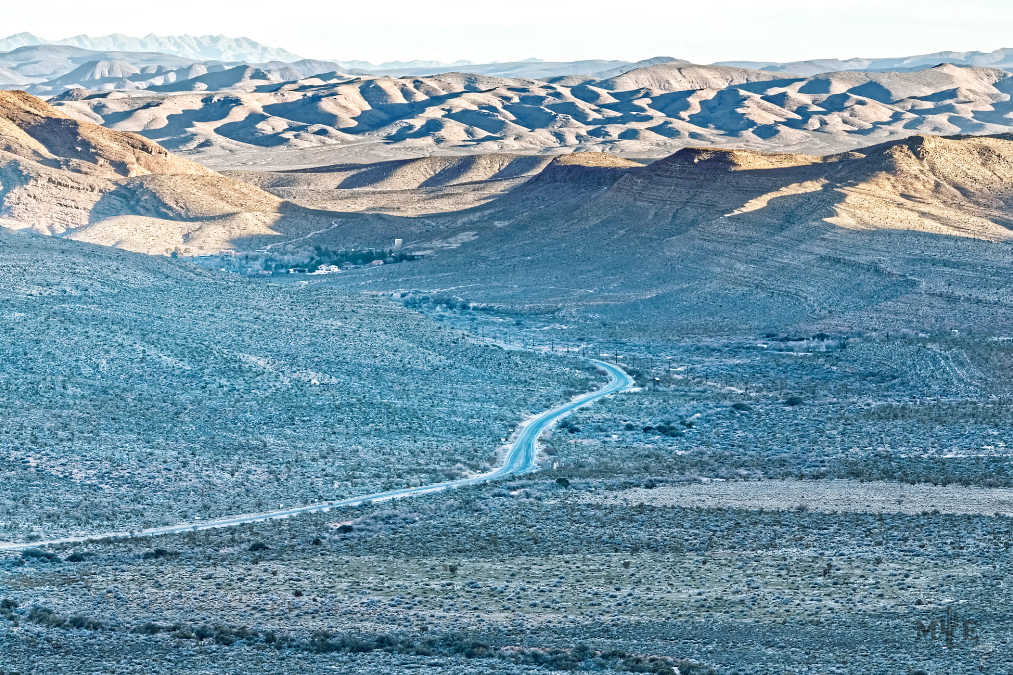 State Route 159 running through a shadow covered Red Rock Canyon East with mountainous dunes in the background.
