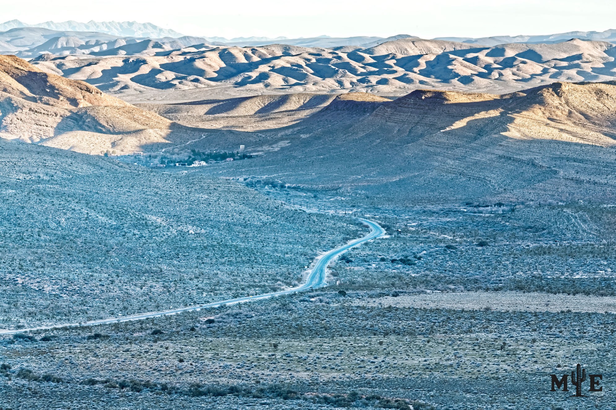 State Route 159 passing through the shadowed eastern side of Red Rock Canyon, with layered sandstone mountains in the distance.
