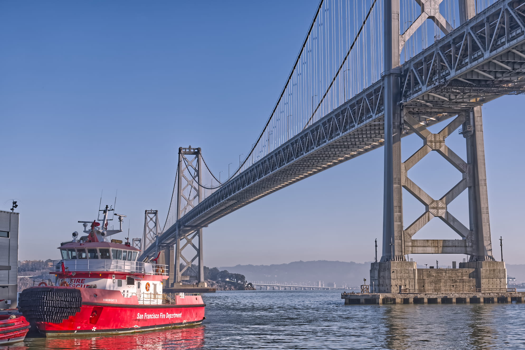 San Francisco Fire Department tug boat floating adjacent to the towering Bay Bridge. Blue sky and pretty day at the bay.