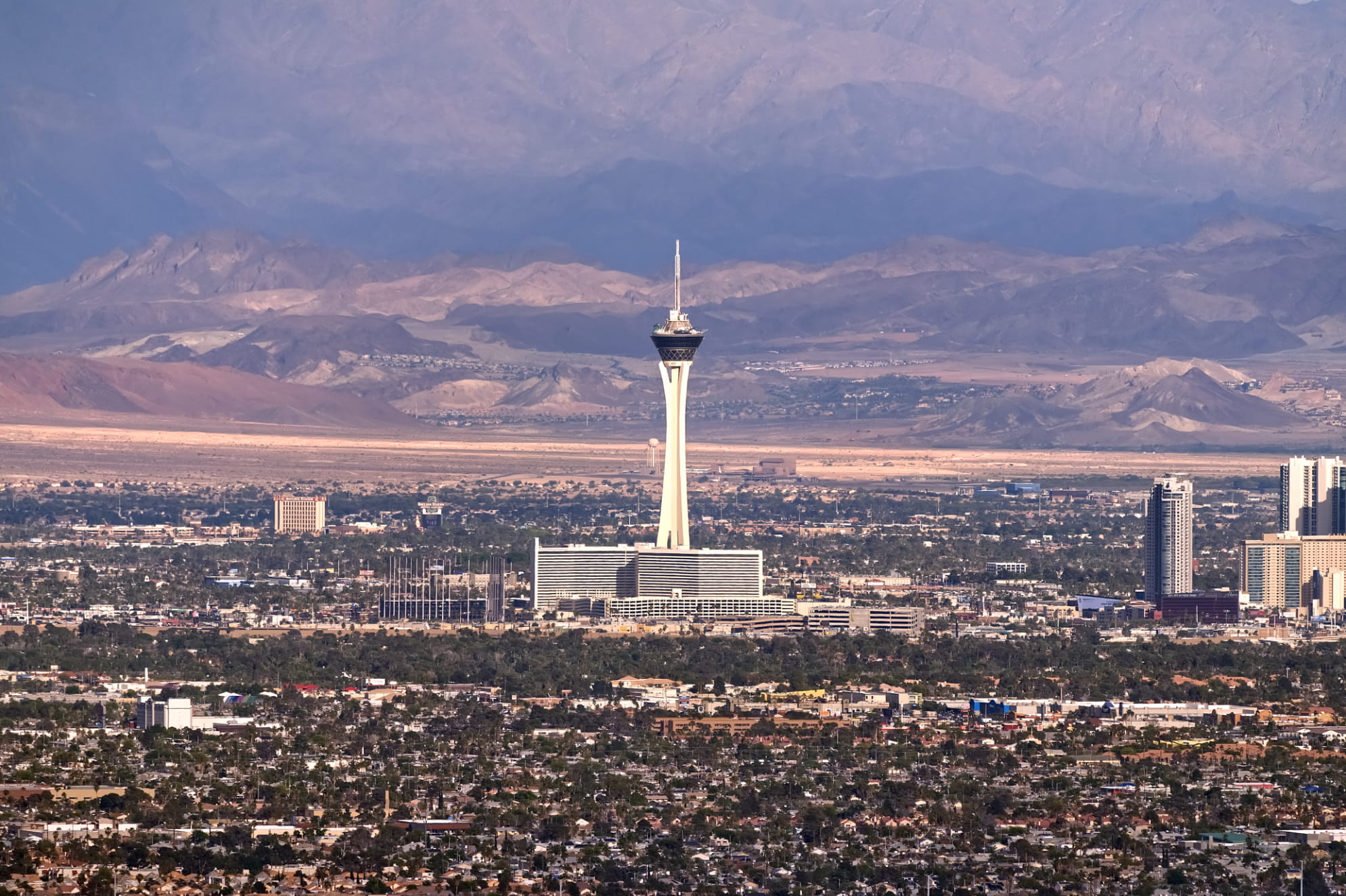 Mountains cover the background of The Stratosphere rising prominently above the Las Vegas Valley with the busy metro area.