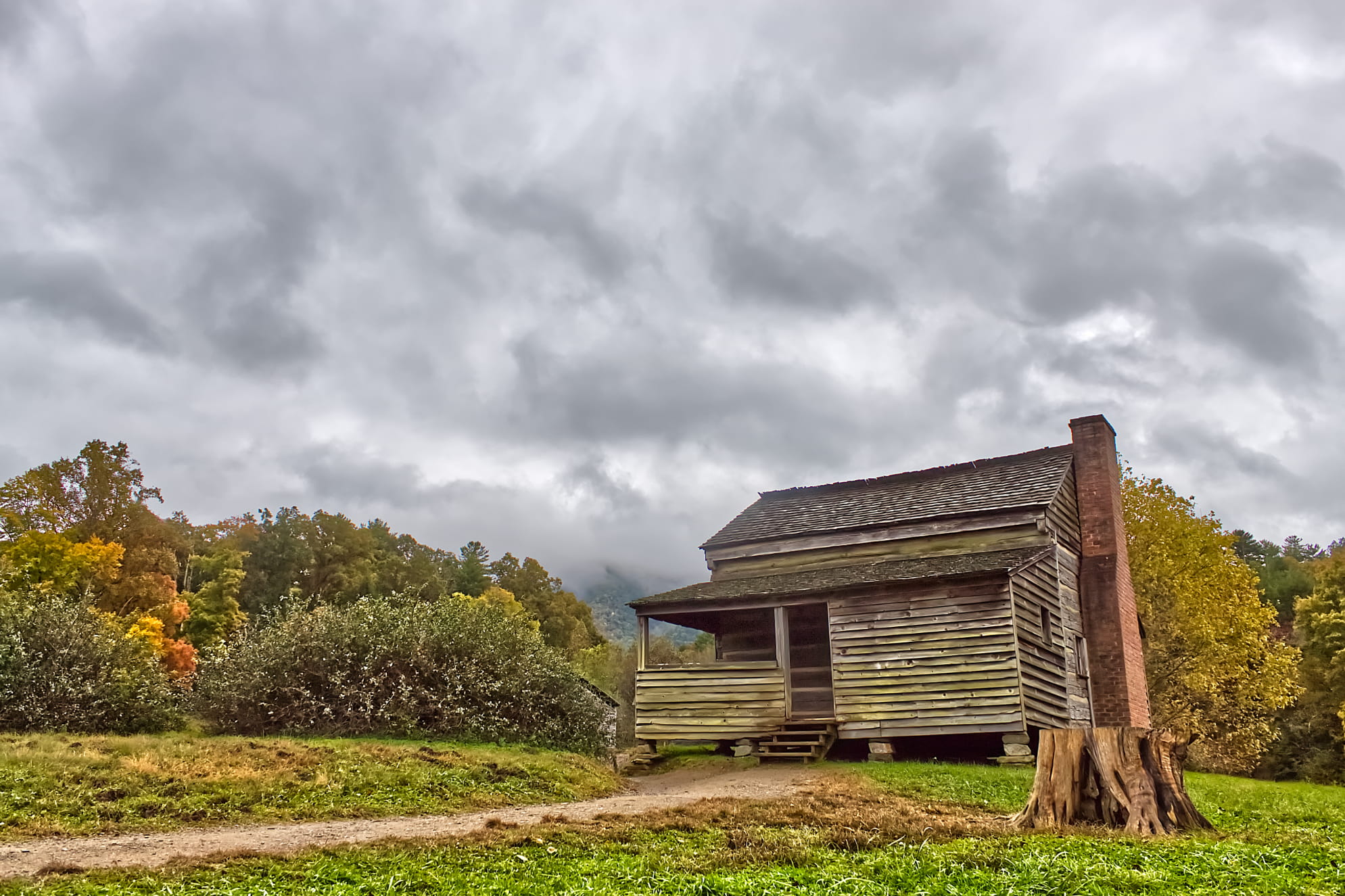 Detailed, overcast clouds with historic civil war era abandoned log cabin. Pathway leading up to it with a tree stump.
