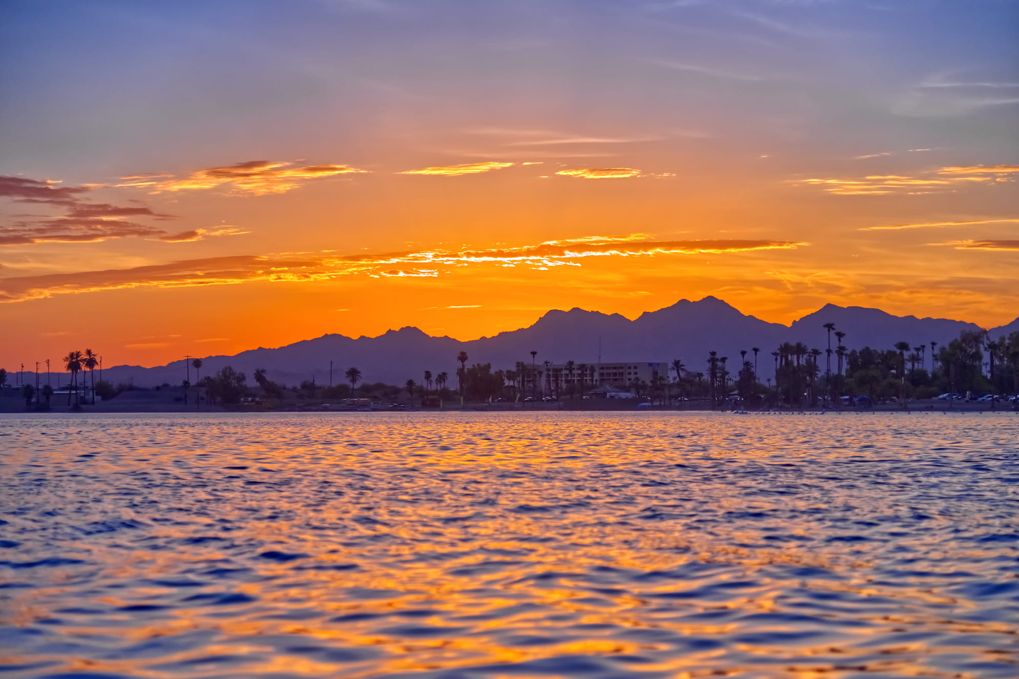 Reflective lake at golden hour with heavenly sunset and sky fading from blue to yellow orange.