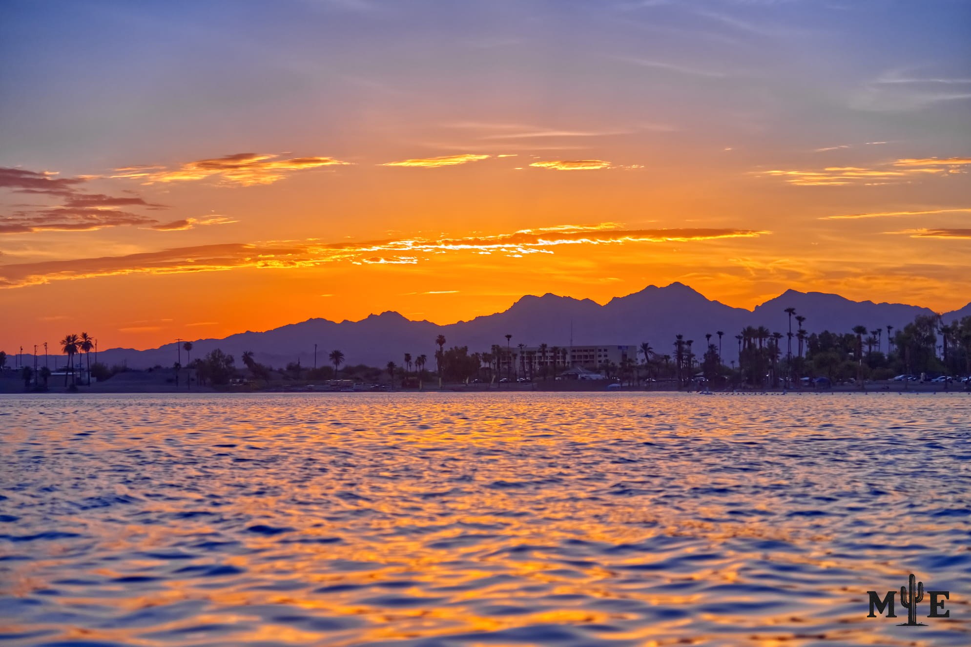 Calm Lake Havasu reflecting a golden-hour sky that fades from blue into yellow and orange above the desert shoreline.