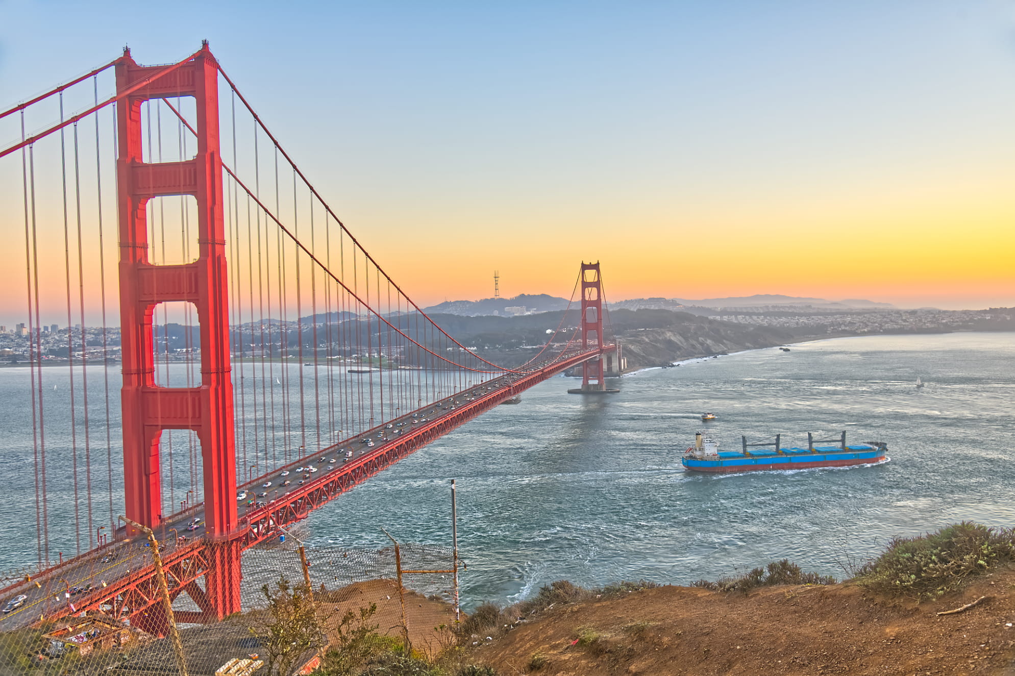 Towering Golden Gate Bridge shot from a mountainside cliff overlook with golden hour sunset and oil tanker crossing the bay.