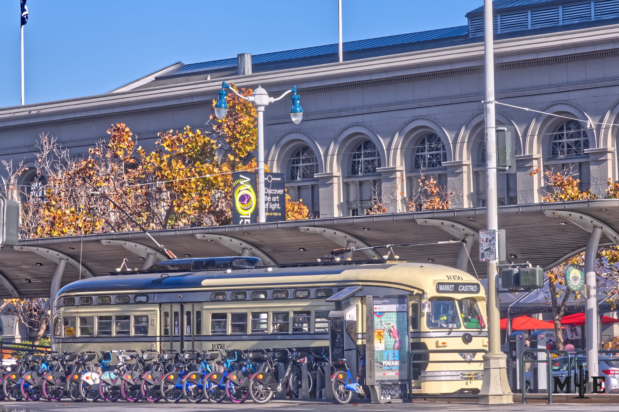 Historic San Francisco trolley car adjacent to terminal with long line of bicycles. Busy metro scene.