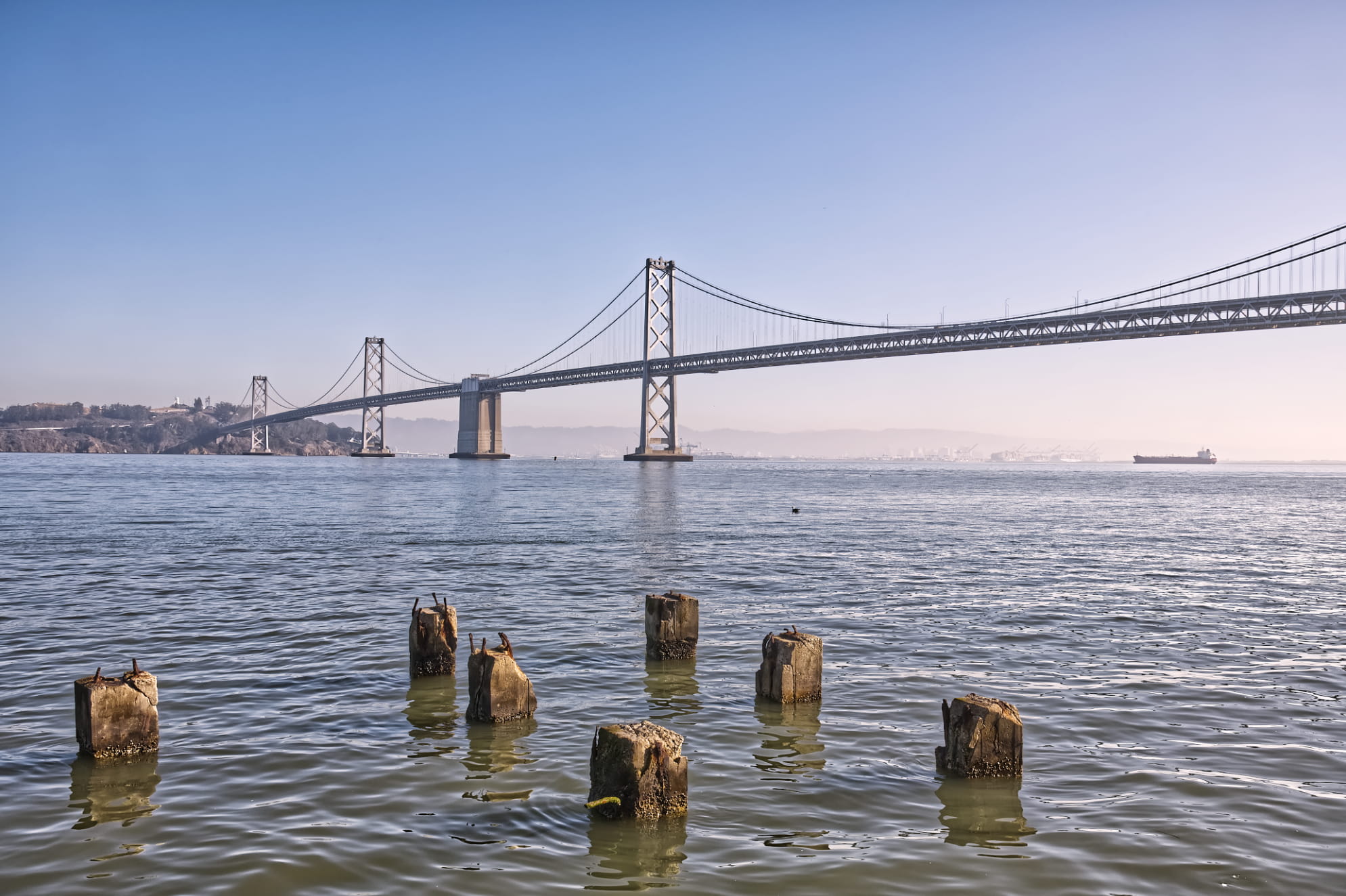 San Francisco Bay Bridge wide angle daytime shot with wooden posts sticking out of the foreground water.