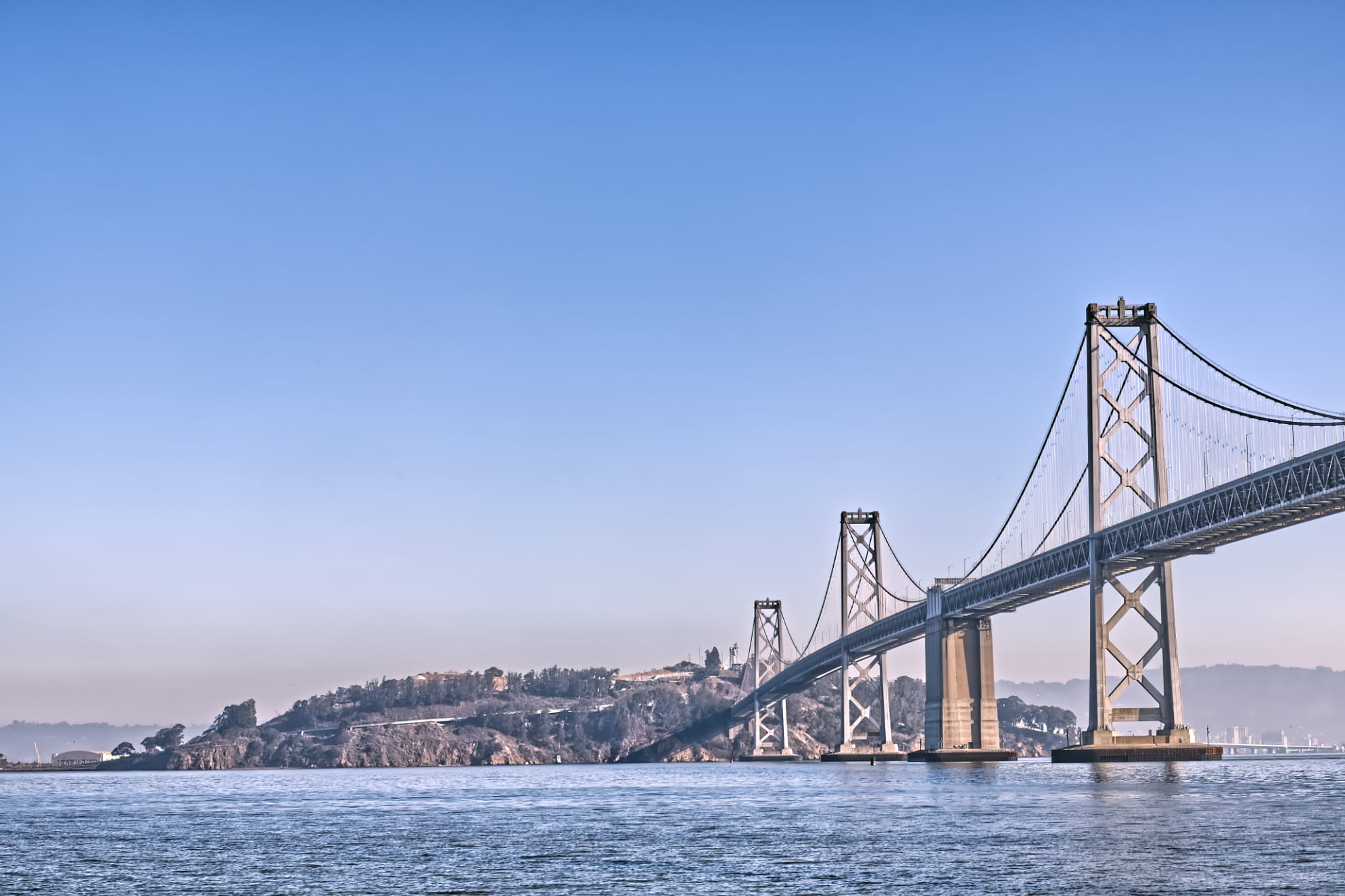 San Francisco Bay Bridge leading directly into Treasure Island on a blue sky day over the blue water bay.