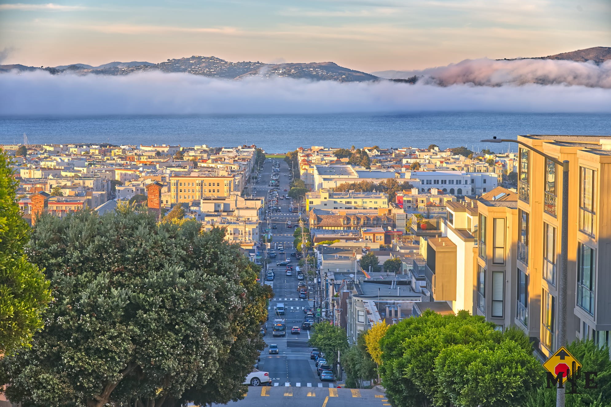 Pacific Heights residential street above San Francisco Bay as dense fog moves into the city and softens the distant view.