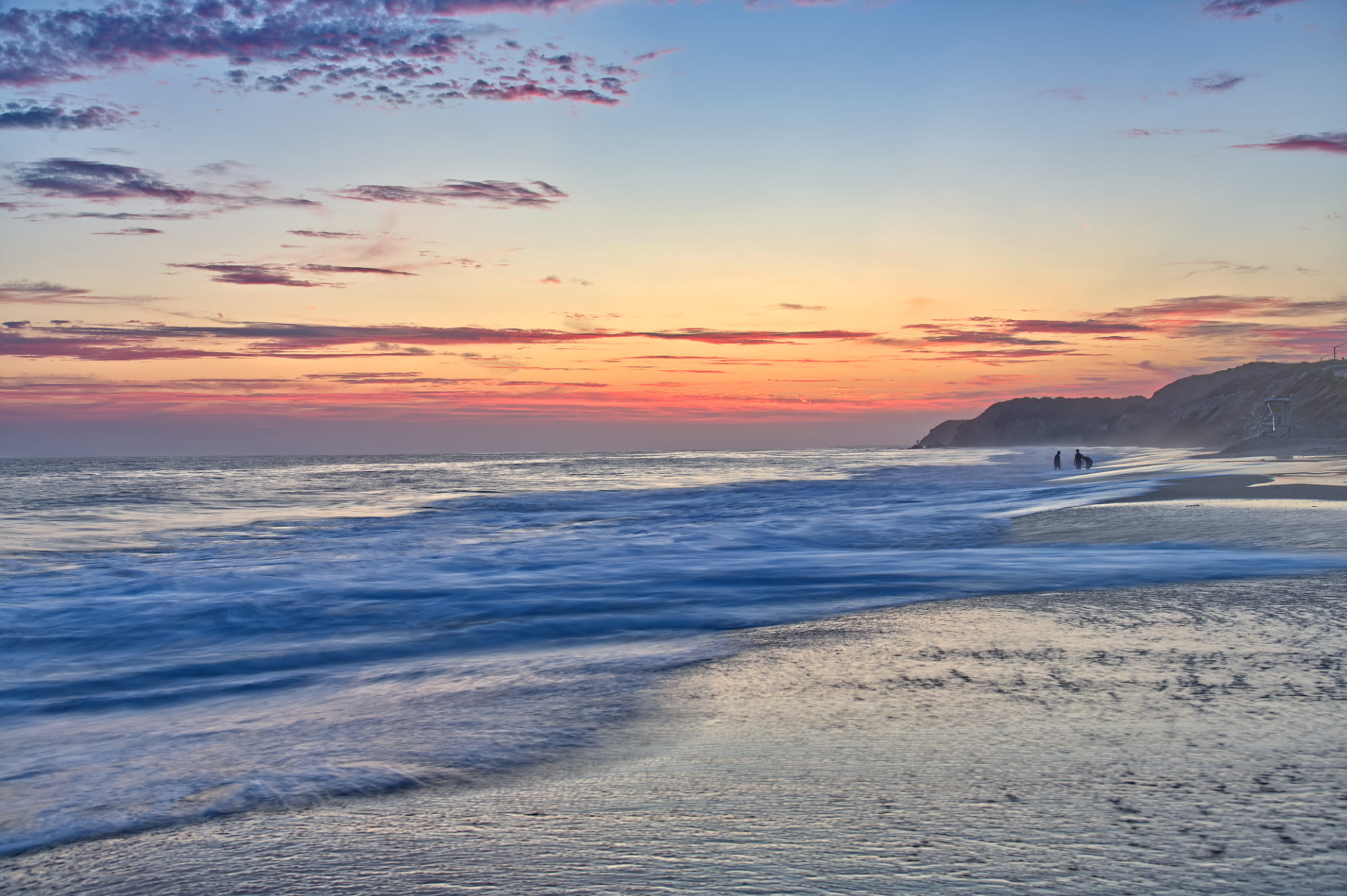 Soothing pastel beach sunset sky with silhouettes in the distance and a dramatic seashore. California beach photograph.