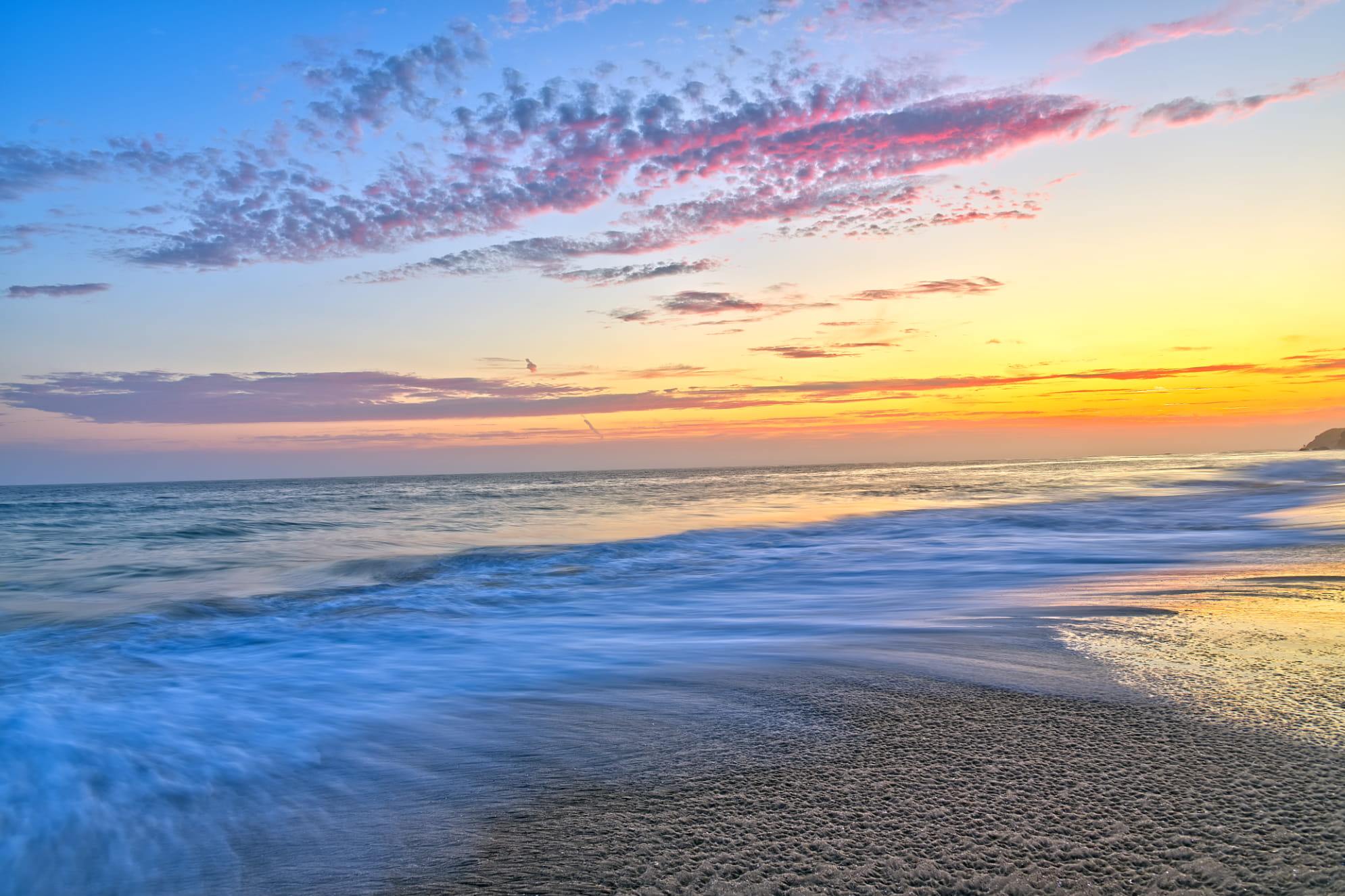 Colorful pastel beach sunset sky with a long exposure seashore. Water is in motion on detailed sandy beach.
