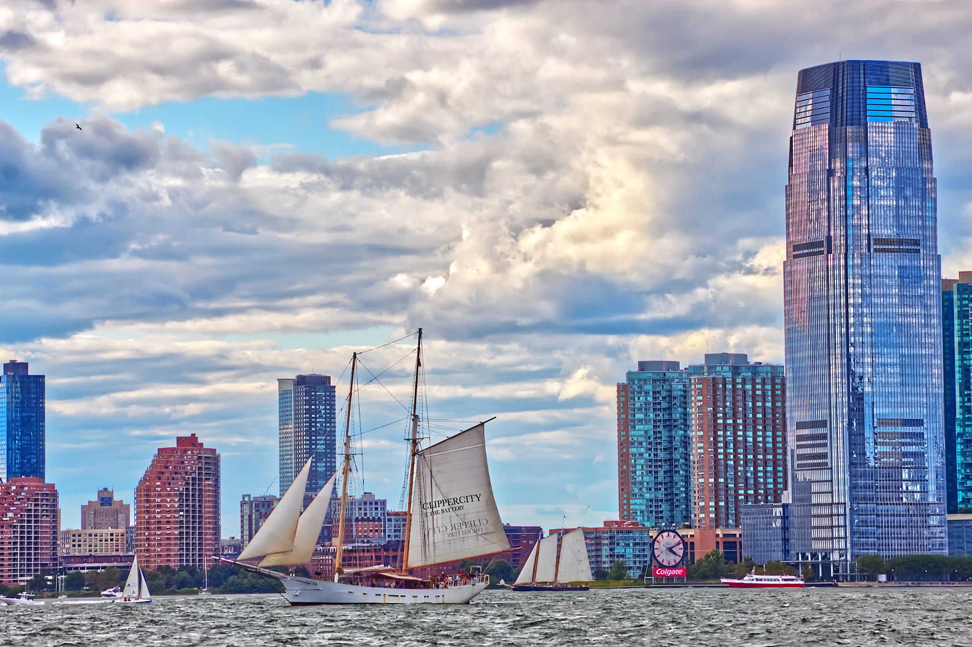 Dramatic clouds over buildings on New Jersey's shoreline with an exotic sale boat on the water. Looks to be a windy day.