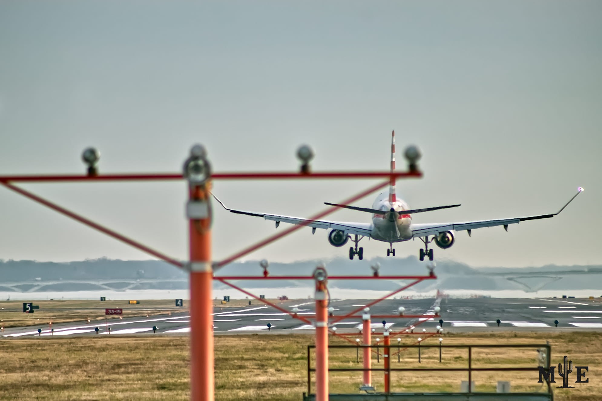 Passenger jet descending toward a Reagan National Airport runway beneath an overcast sky, framed by runway lights, posts and airport infrastructure.