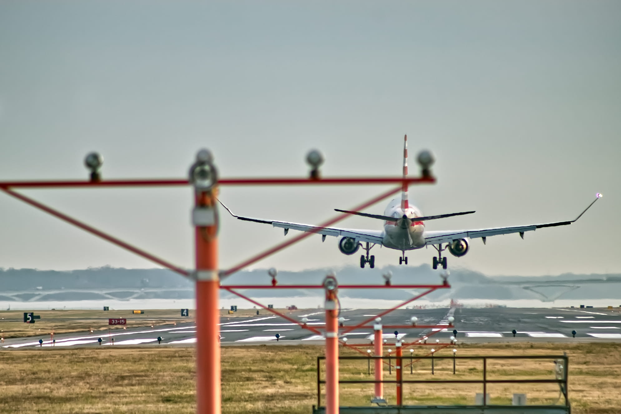 Passenger landing on a runway with airport posts, poles and lights emanating from the airplane. Overcast day.