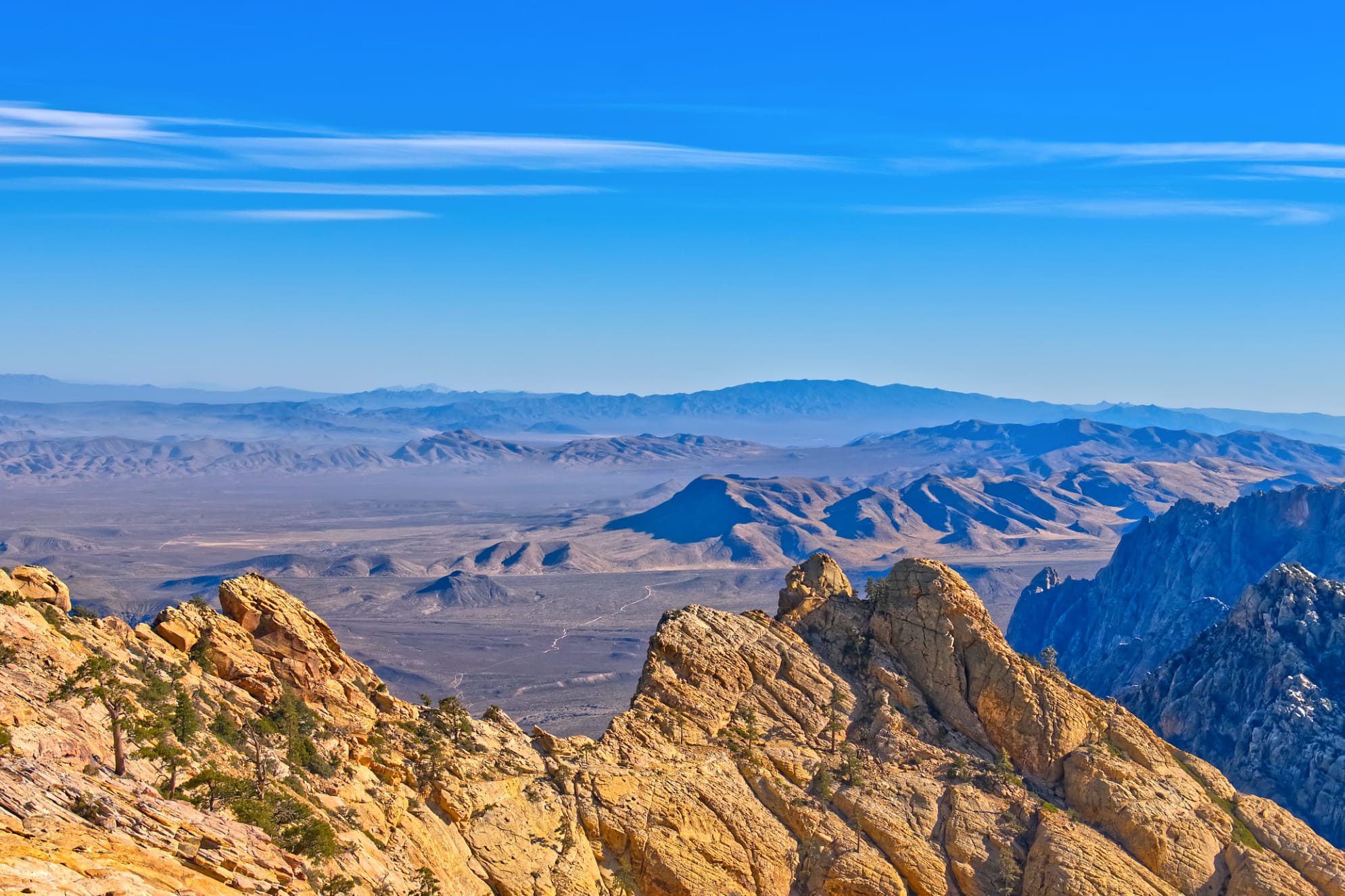 Blue sky and infinite desert overlook with jagged mountains and golden sunset, sandstone mountain peaks.