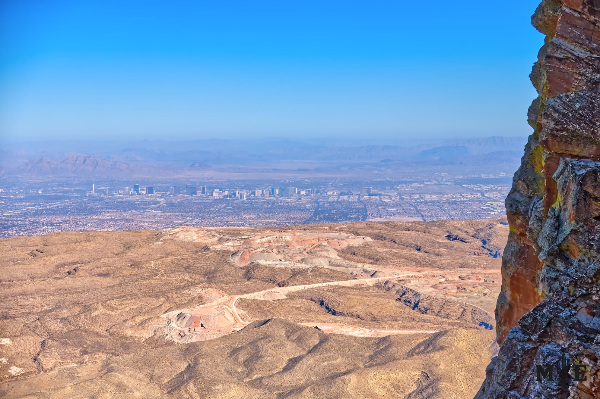 Rugged Red Rock Canyon mountain edge above a vast desert basin, with the Las Vegas metropolitan area visible in the distance.