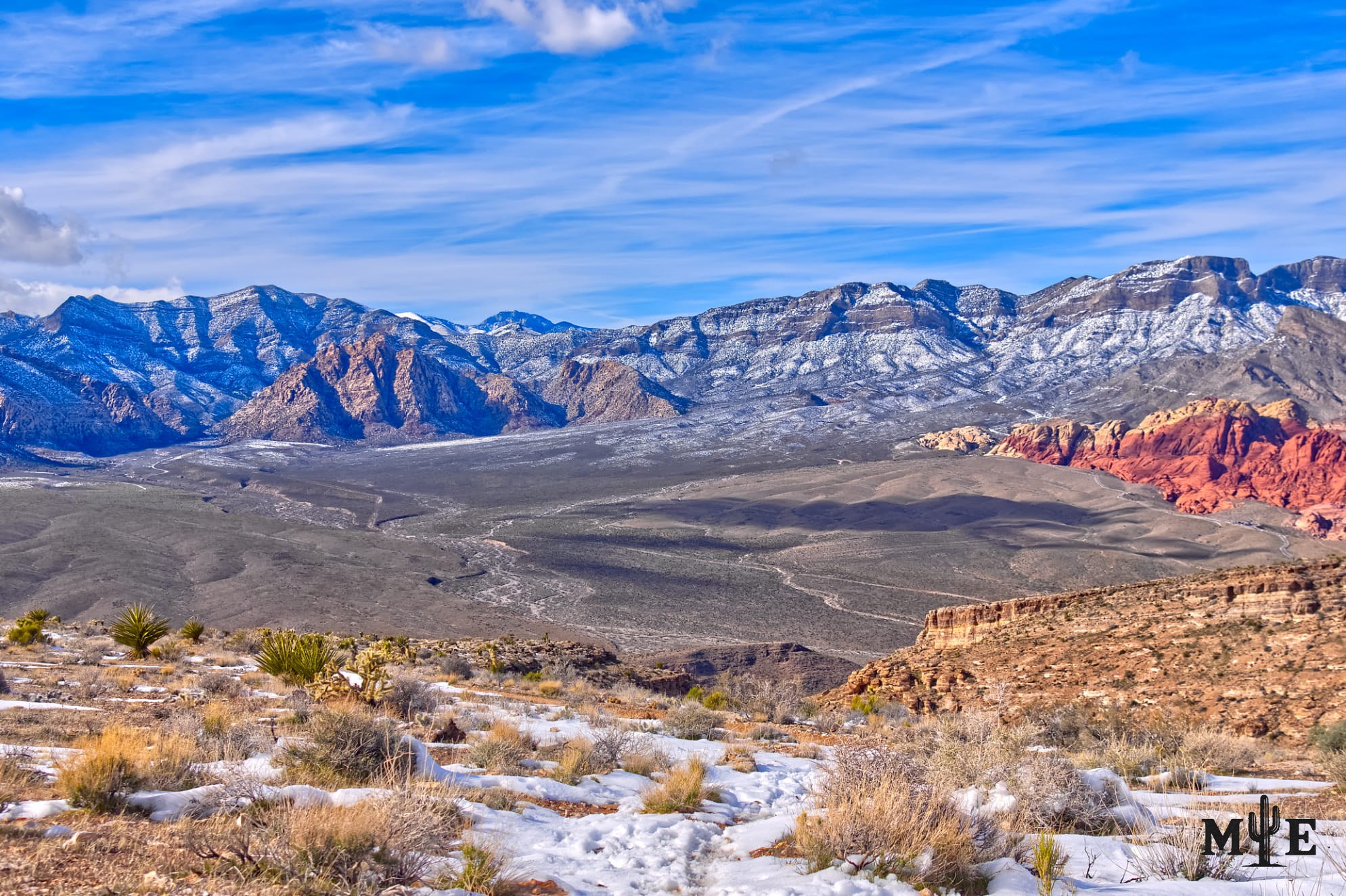 Vibrant blue winter sky above lightly snow-covered Spring Mountains and scattered snow across the Red Rock Canyon desert foreground.