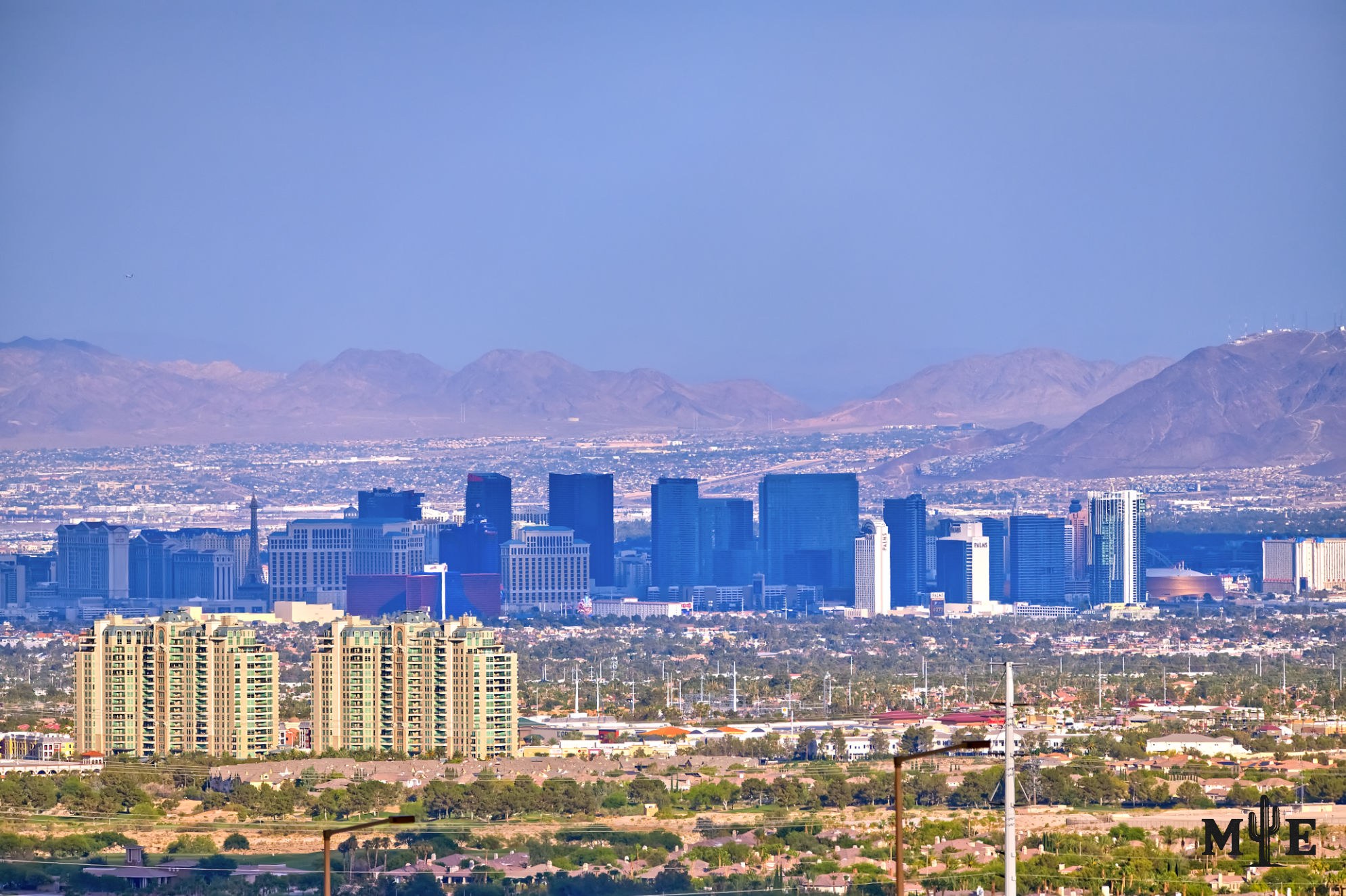 Telephoto view from Sun City Summerlin across the Las Vegas Valley toward the Strip, partly shaded beneath passing clouds.