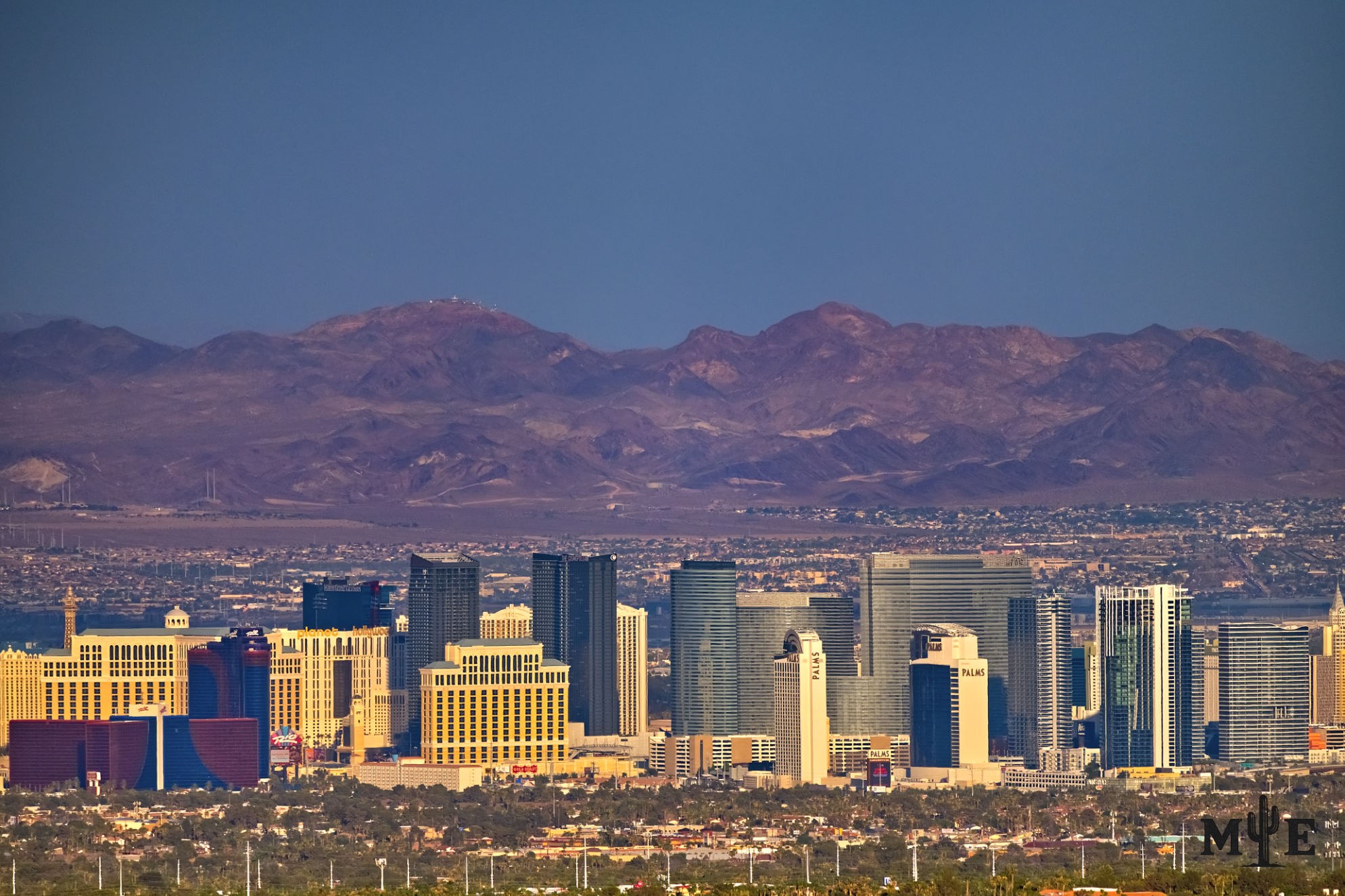 Densely packed collection of Las Vegas resorts near dusk with mountains in the background and city life afront.