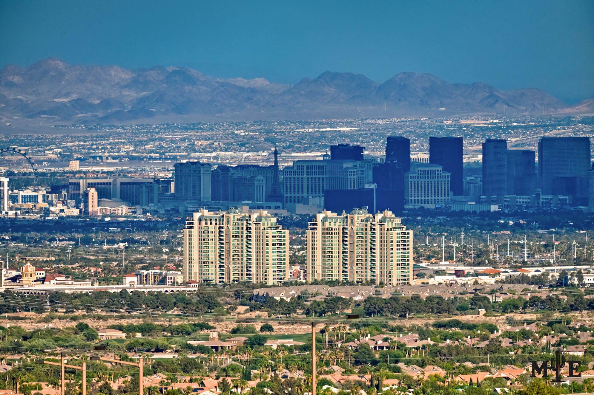 The twin towers of One Queensridge Place in the foreground, with the Las Vegas Strip beneath a passing cloud in the distance.