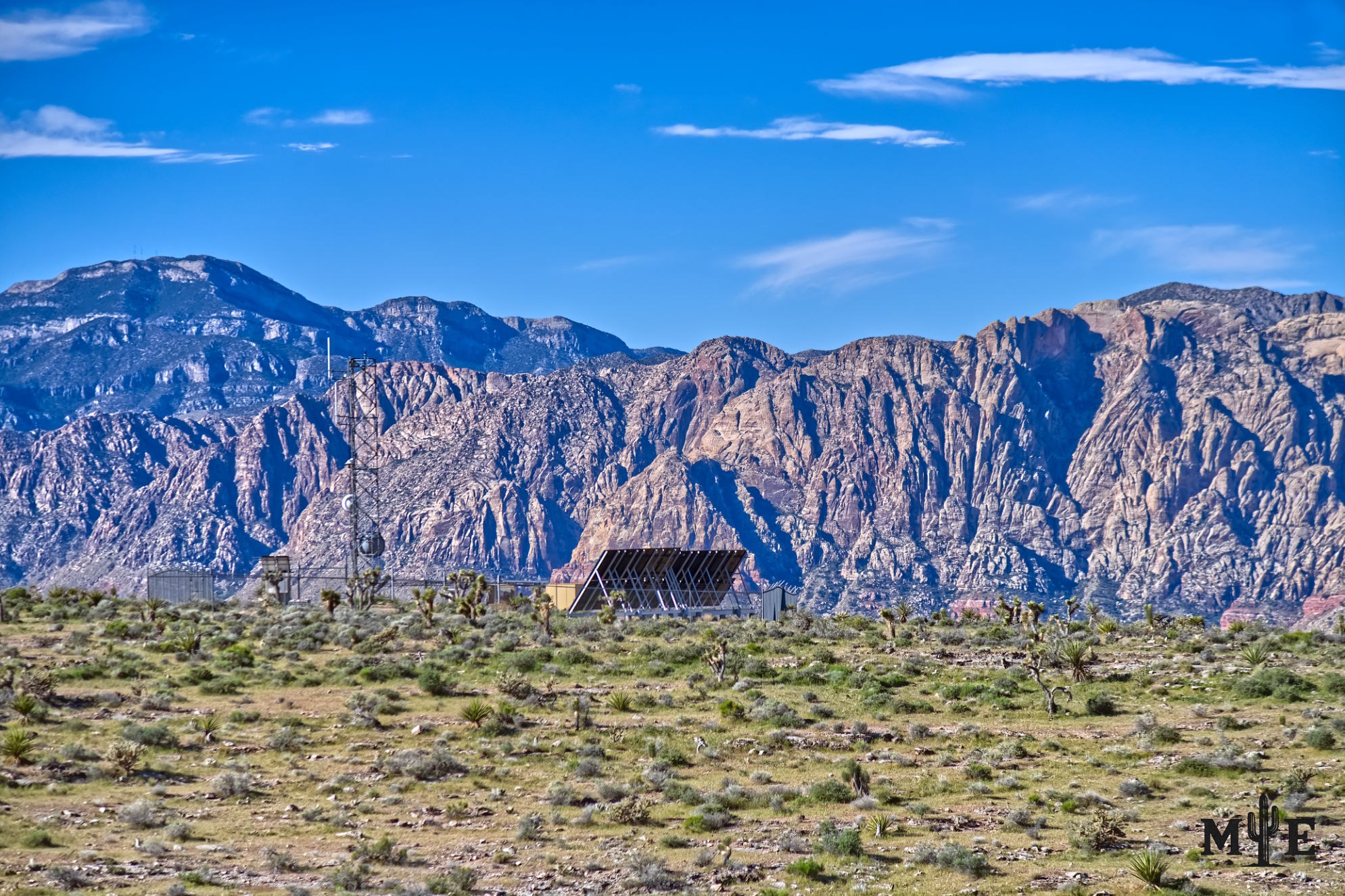A radio tower rising from desert terrain beneath the Spring Mountains and a clear blue Las Vegas sky.