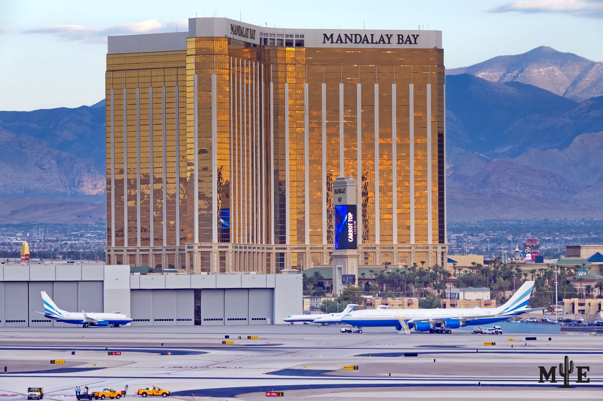 Parked passenger jets at Harry Reid Intl. Airport with the golden Mandalay Bay towers, blue sky & dramatic mountains beyond.