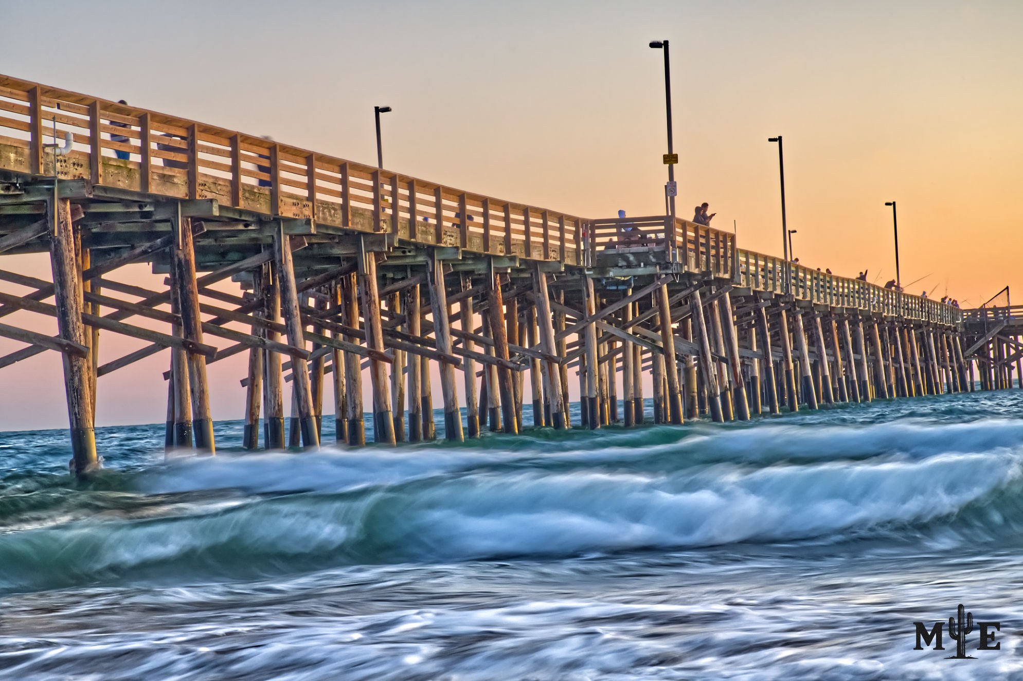 long exposure of the historic wood pilings at the Newport Beach Pier as soft ocean waves rush beneath it at sunset.